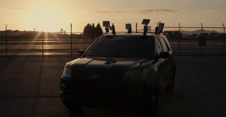 LDG surveillance vehicle with roof cameras parked behind a fenced site at sunset